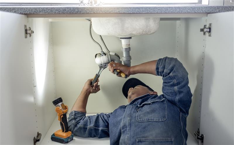 Plumber repairing pipes beneath a bathroom sink in The Villages