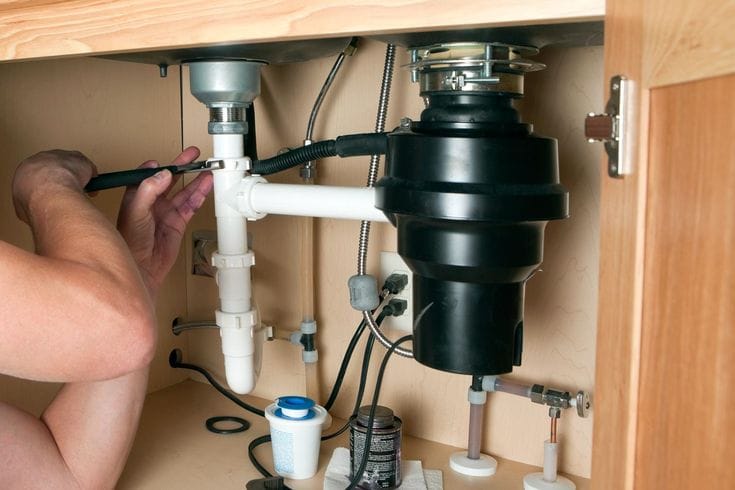 Plumber installing a garbage disposal beneath a kitchen sink in The Villages