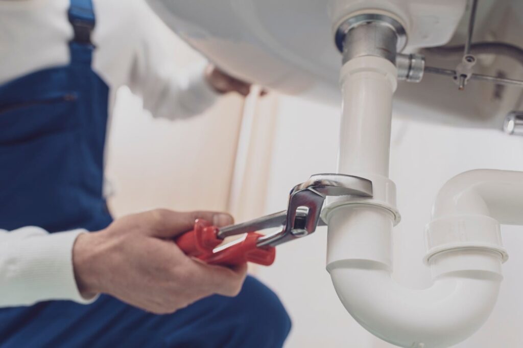 Plumber repairing a white drain pipe beneath a sink in The Villages