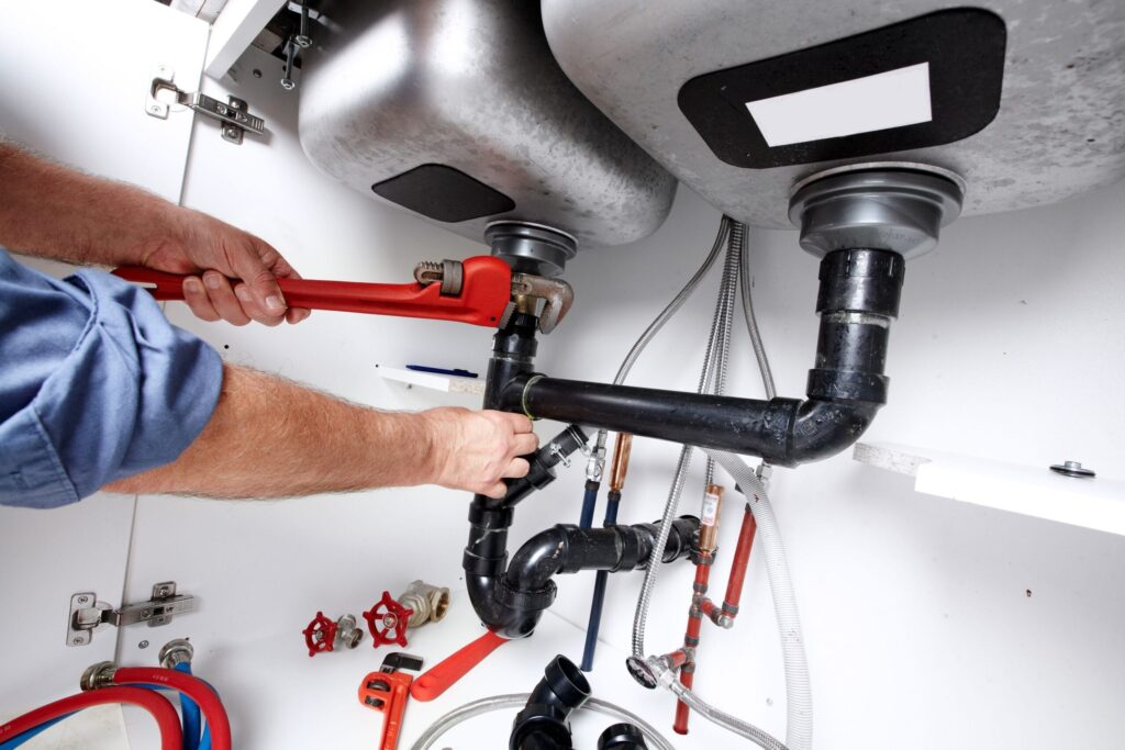 Plumber repairing drain pipes beneath a kitchen sink in The Villages